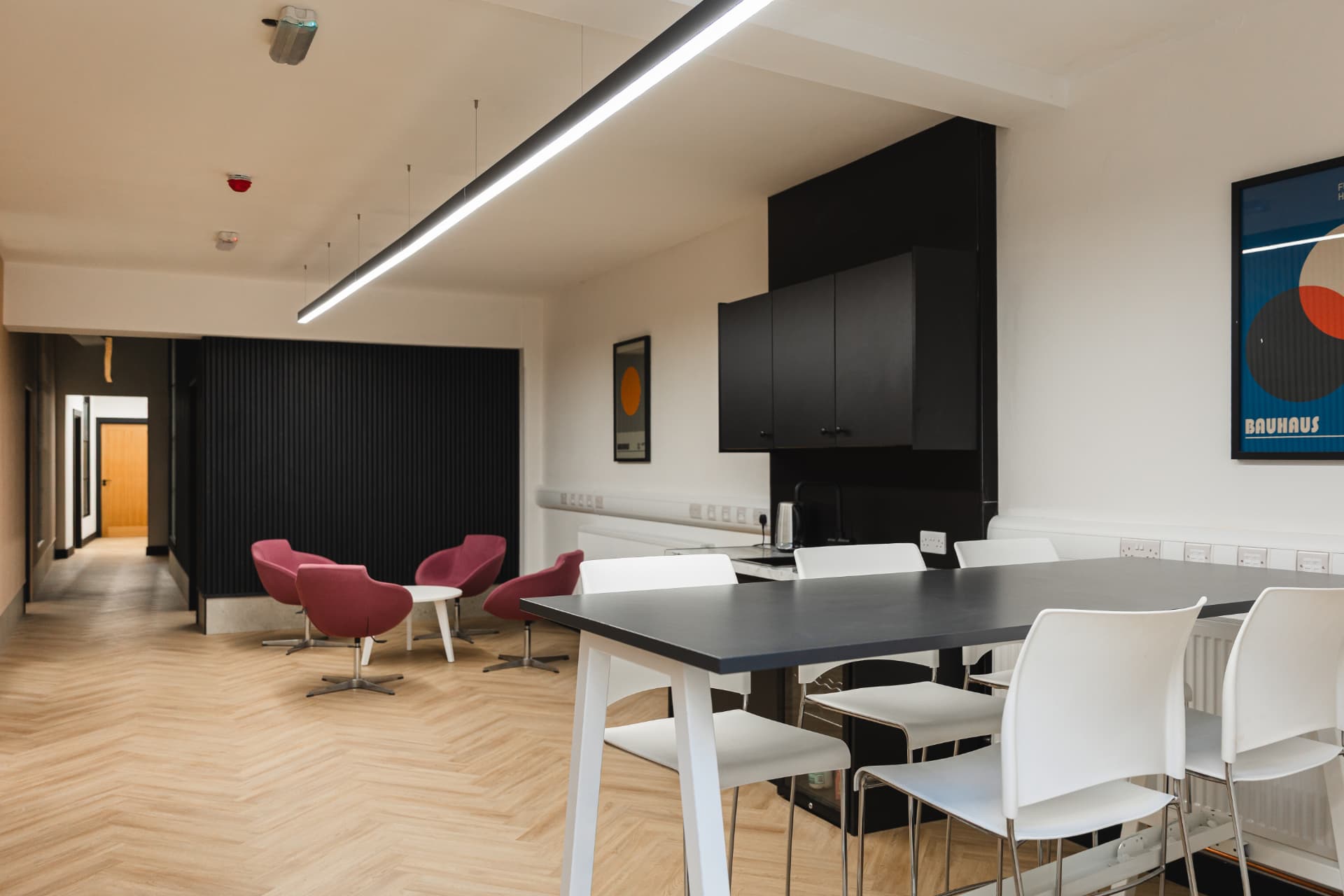 Modern kitchen and breakout area at Workpoint with black cabinets, pink armchairs and high tables