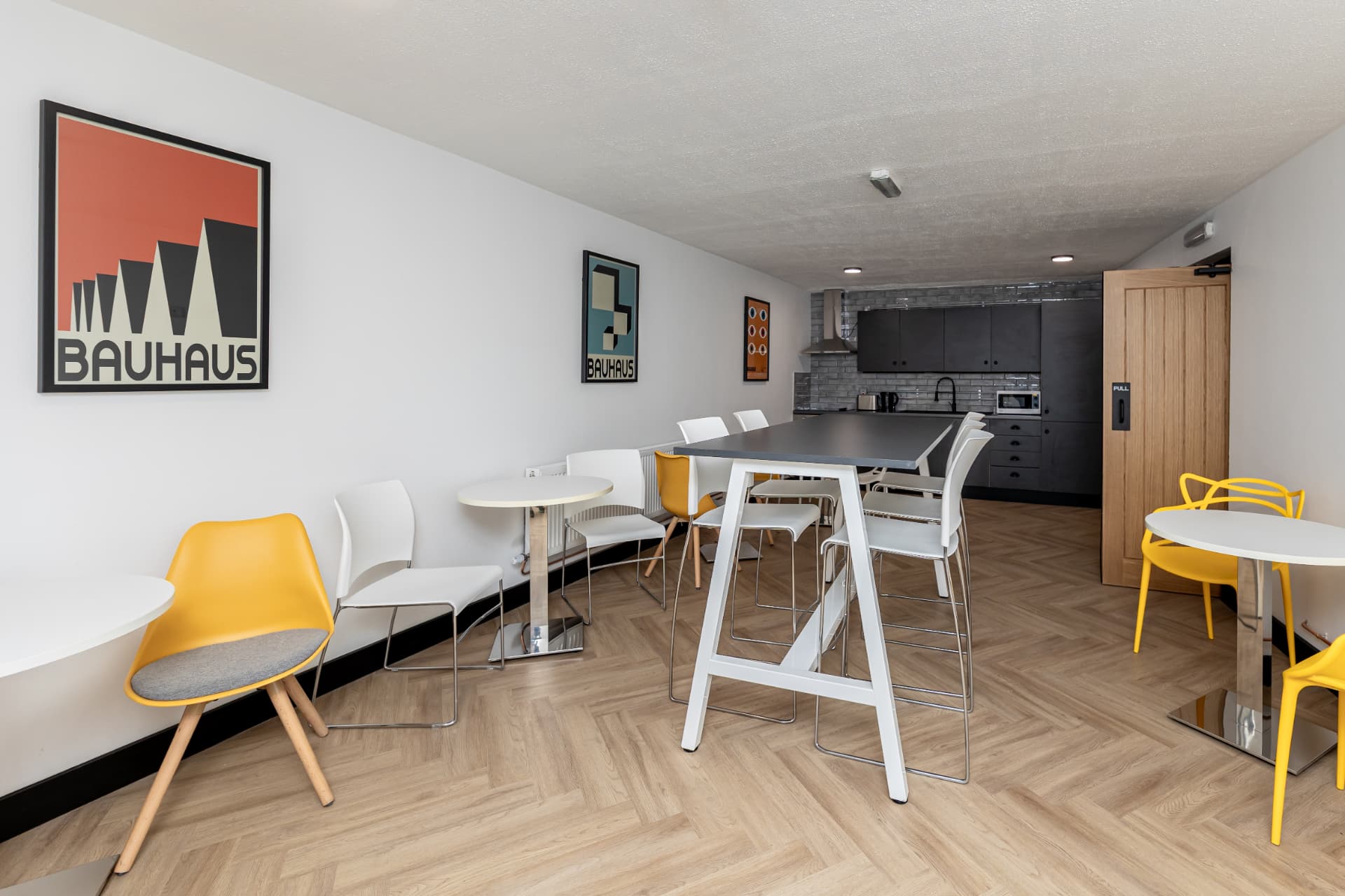 Bright kitchen and breakout area at Workpoint with Bauhaus prints, high tables, and yellow chairs