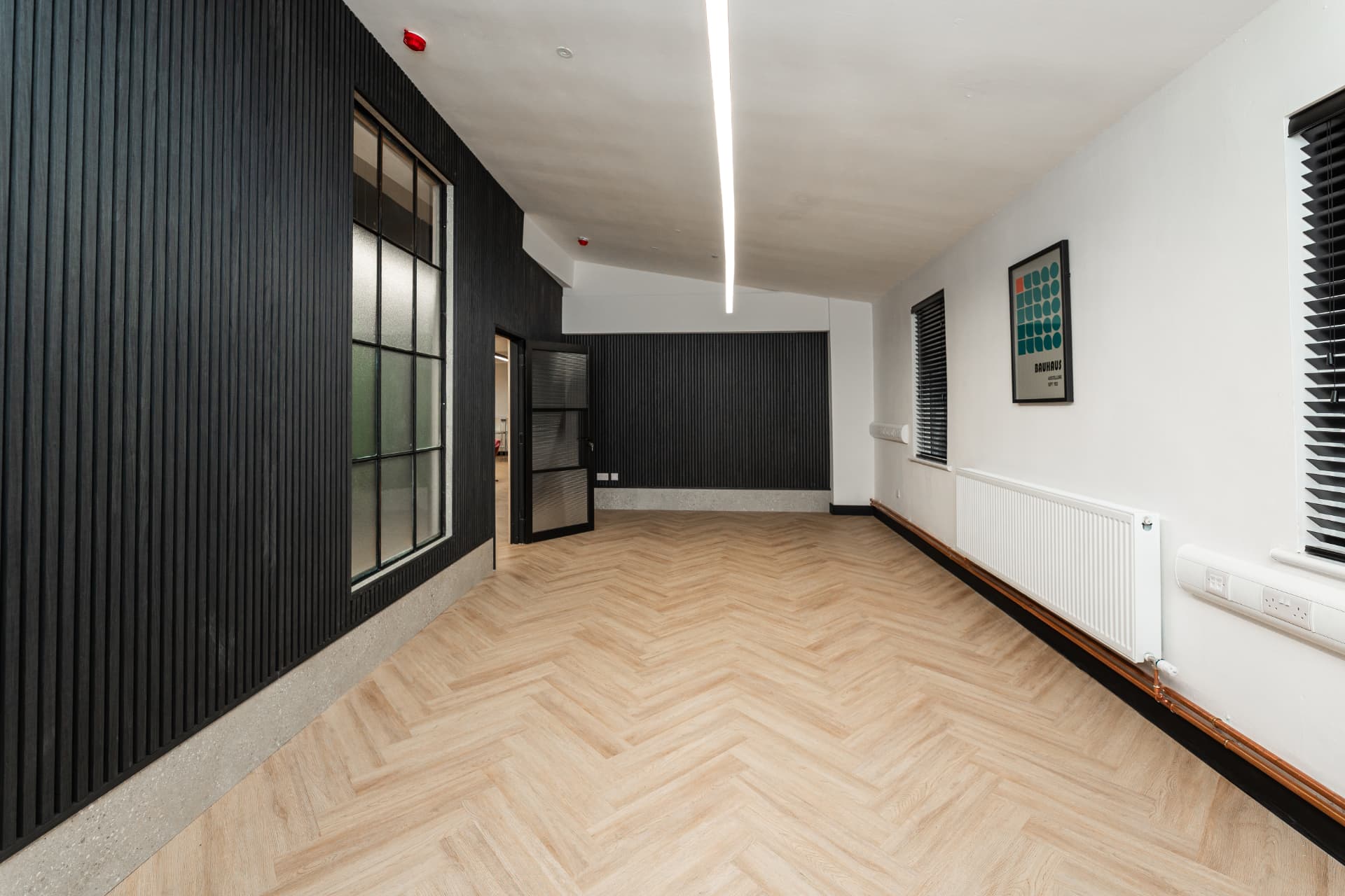 Large private office at Workpoint with black slatted walls, herringbone flooring and feature lighting